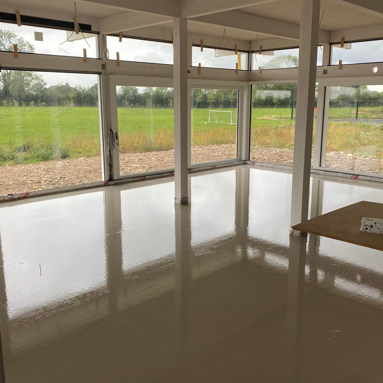 Glossy freshly poured liquid screed covering the floor of a room with floor-to-ceiling windows