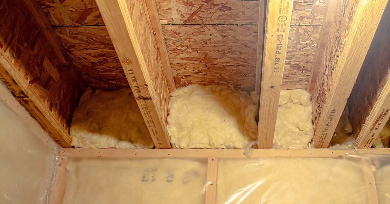 Underside of an OSB subfloor carried on I-joists, with fiberglass insulation between them