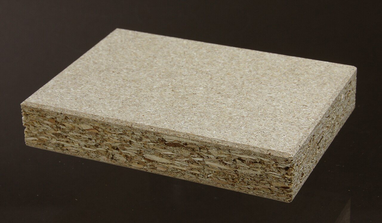 Block of particle board on a dark background showing its compressed wood-chip core
