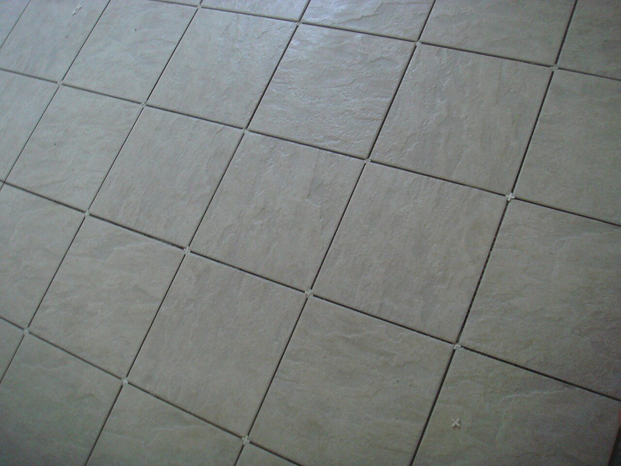 Newly laid light ceramic floor tiles with small cross spacers still visible in the joints