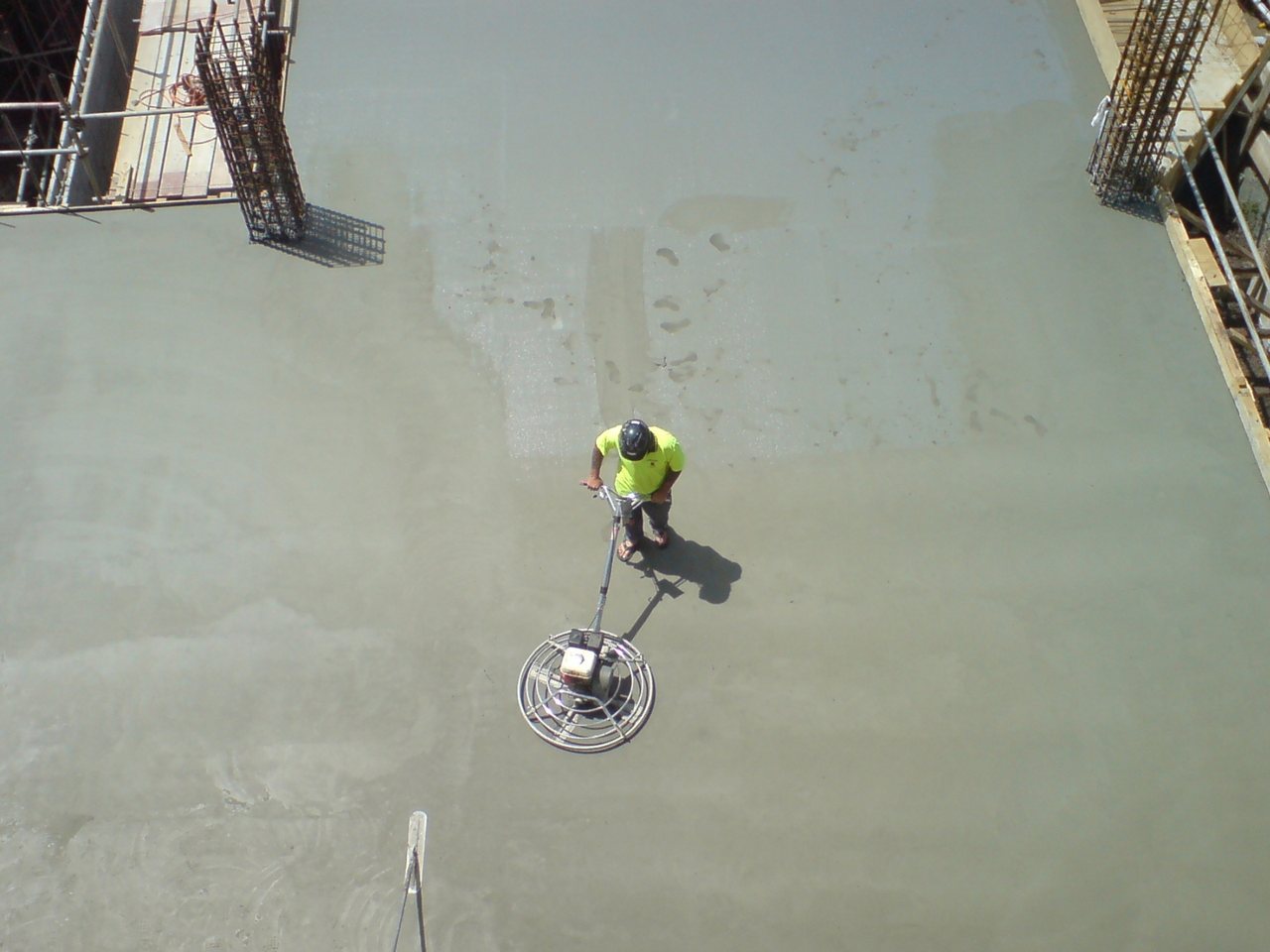 Overhead view of a worker running a power trowel across a large fresh concrete slab