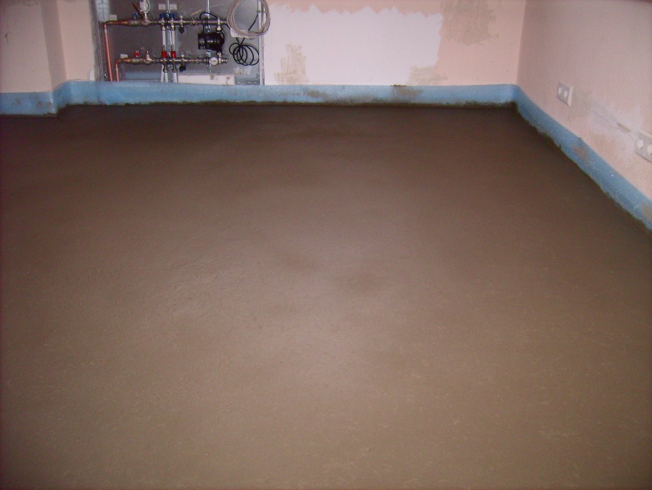 Freshly laid sand-cement screed covering a room floor, with blue edge insulation strip along the walls
