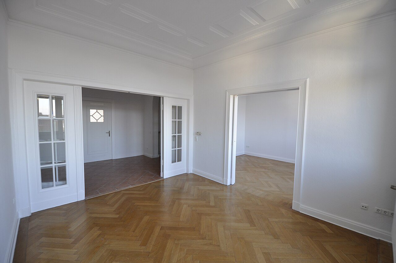Empty renovated apartment with an oak herringbone floor meeting a tiled floor at an open double doorway