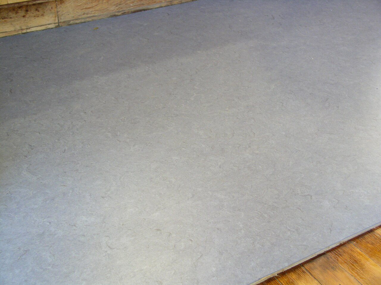 Grey marbled linoleum floor meeting a wooden floor along a metal edge strip
