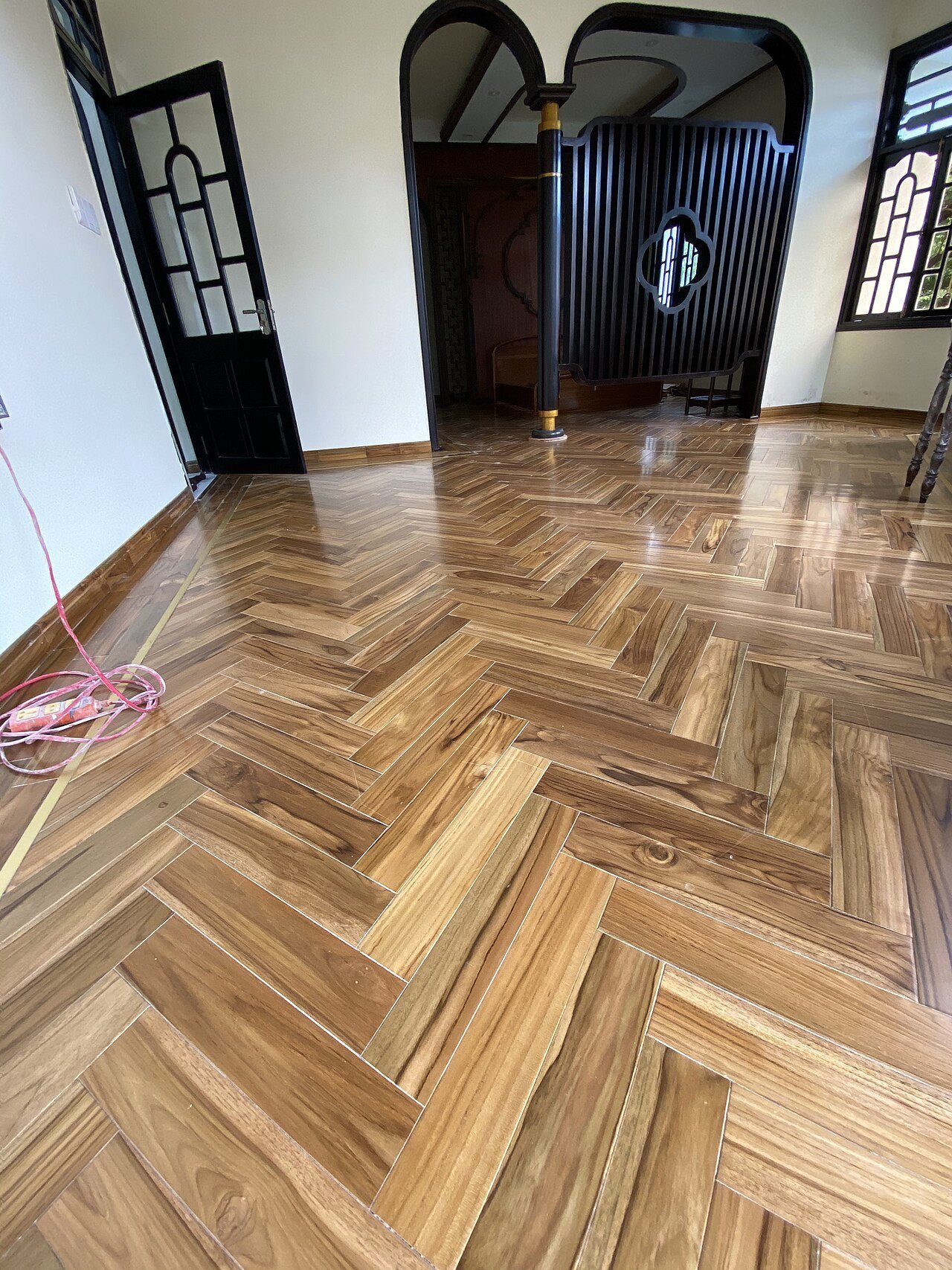 Glossy teak herringbone floor with a thin brass strip along one wall, in a room with arched doorways