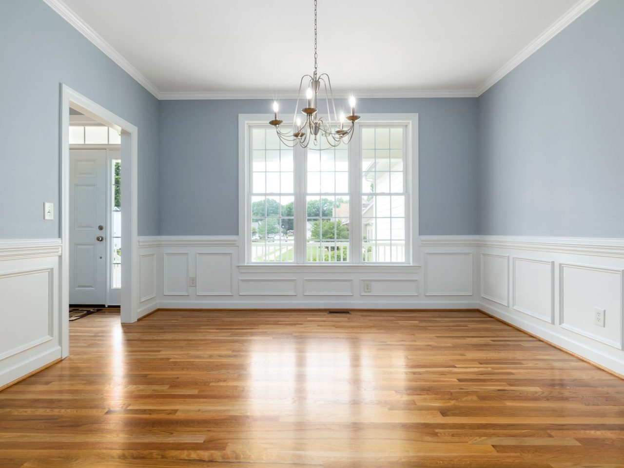 Empty room with white wainscoting, a chandelier and a wood floor