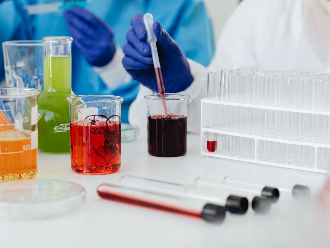 Gloved hands working with laboratory glassware and colored liquid samples