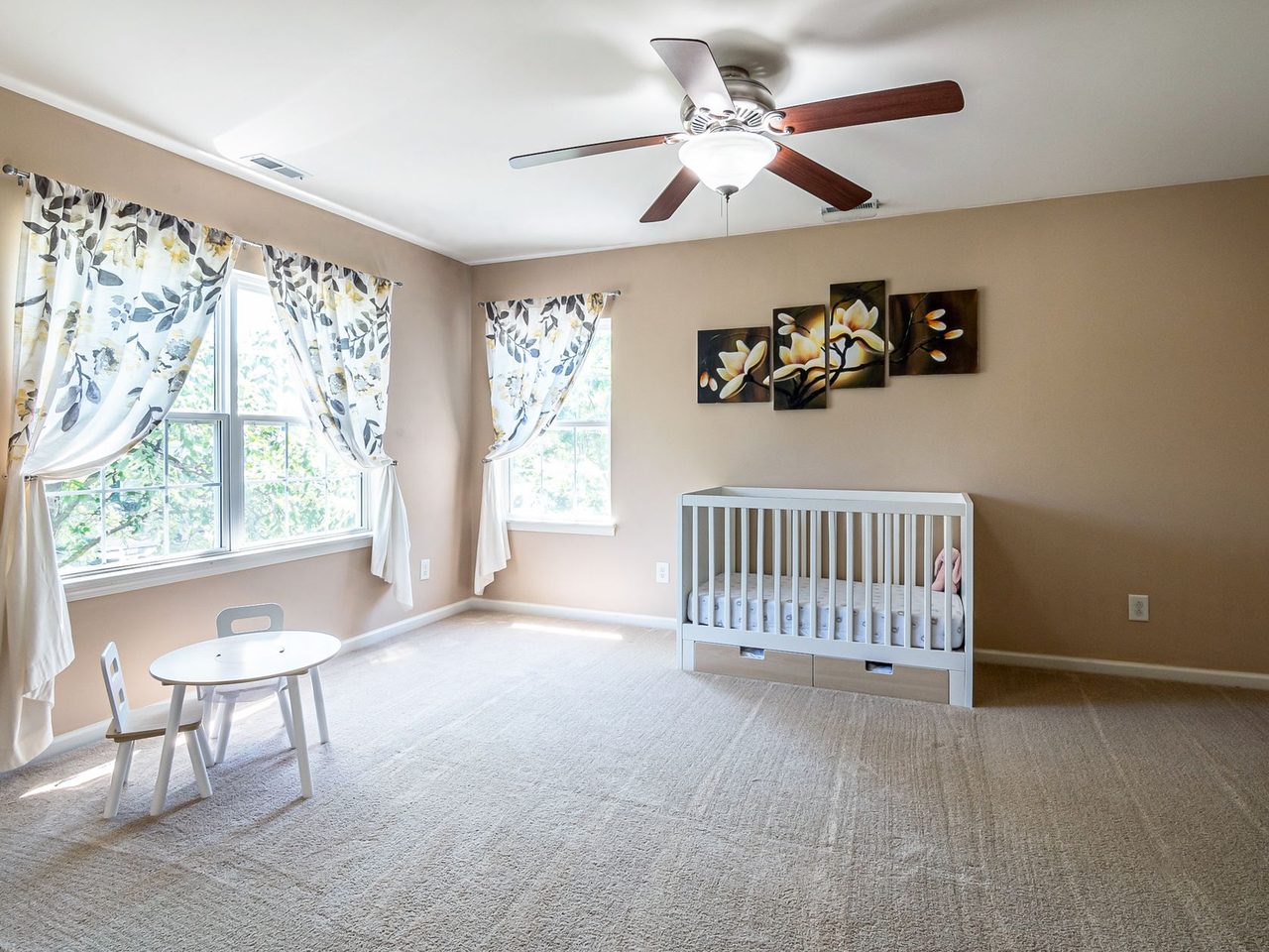 Carpeted nursery room with a crib, a small table and windows