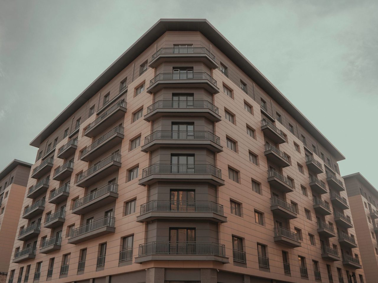 Corner of a multi-story residential building with balconies against a cloudy sky