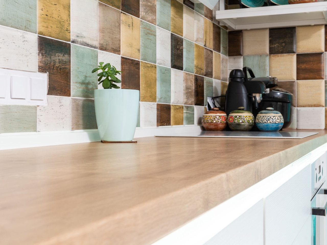 Light kitchen counter below a multicolored tiled backsplash