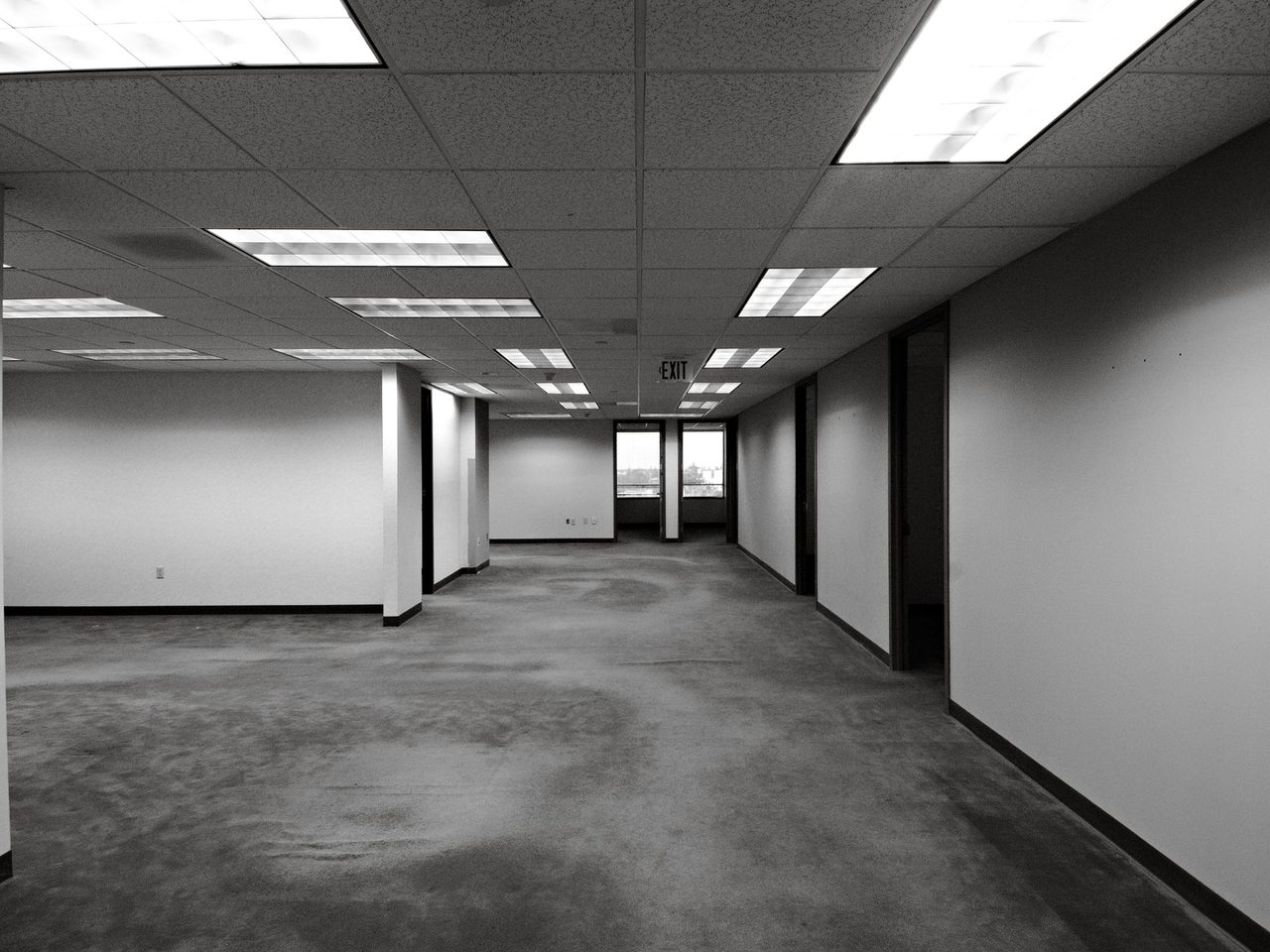 Black and white view of an empty carpeted office under fluorescent lights