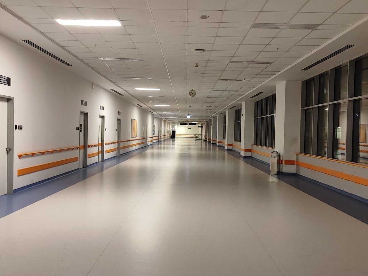 Long hospital corridor with wall base, an orange handrail and a light vinyl floor
