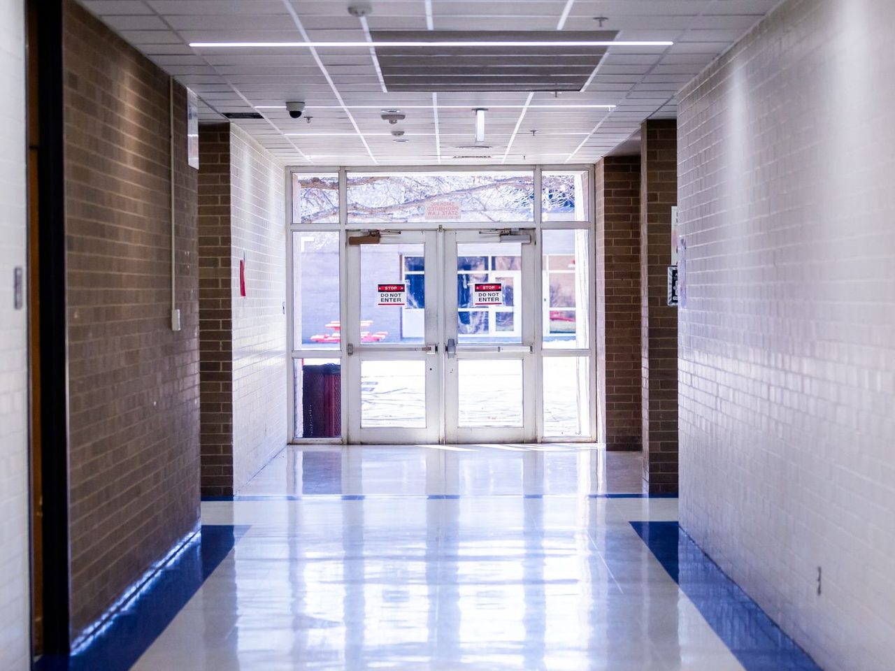 School hallway with a polished floor and blue border leading to glass exit doors