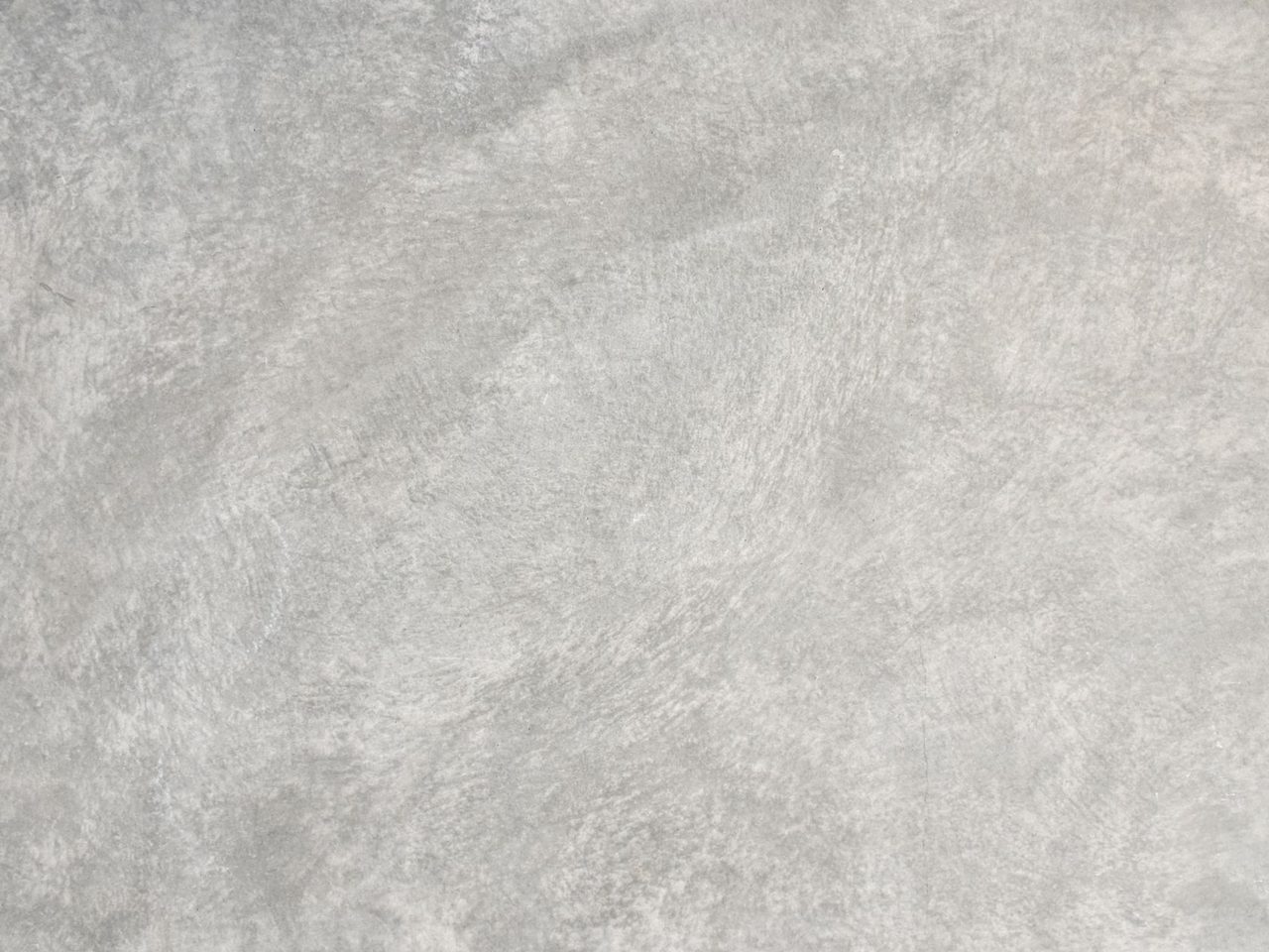 Close-up of a flat gray concrete surface with light and dark mottled patches and a fine, uneven texture.