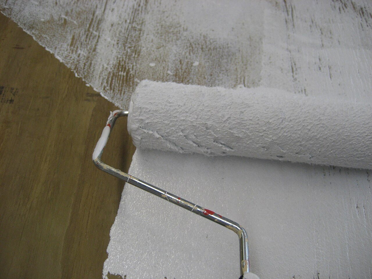 Paint roller spreading white primer across a plywood panel