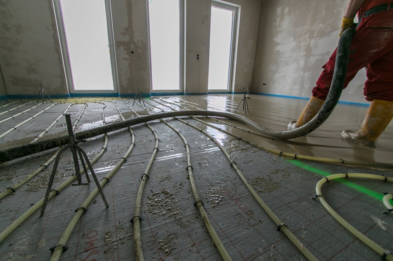 Hose pumping liquid screed over underfloor heating pipes laid on insulation in a new room