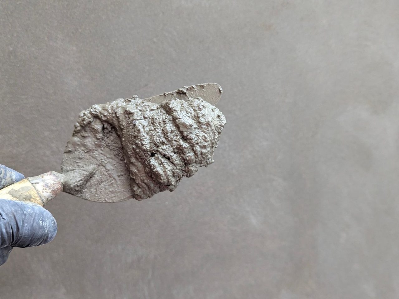 Gloved hand holding a trowel loaded with cementitious material