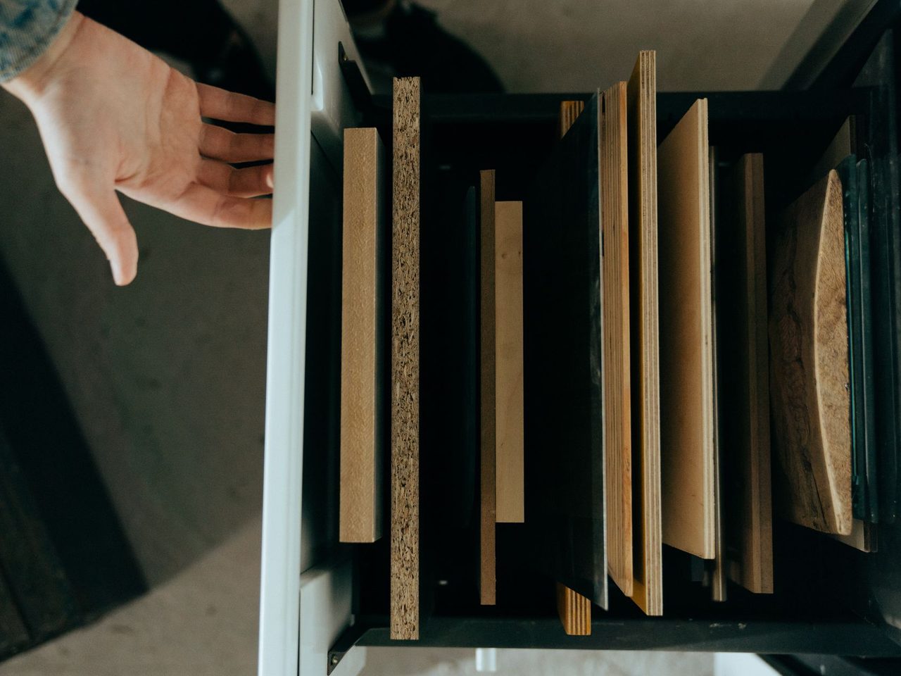 Assorted flooring and panel samples stood on edge in a drawer with a hand reaching in