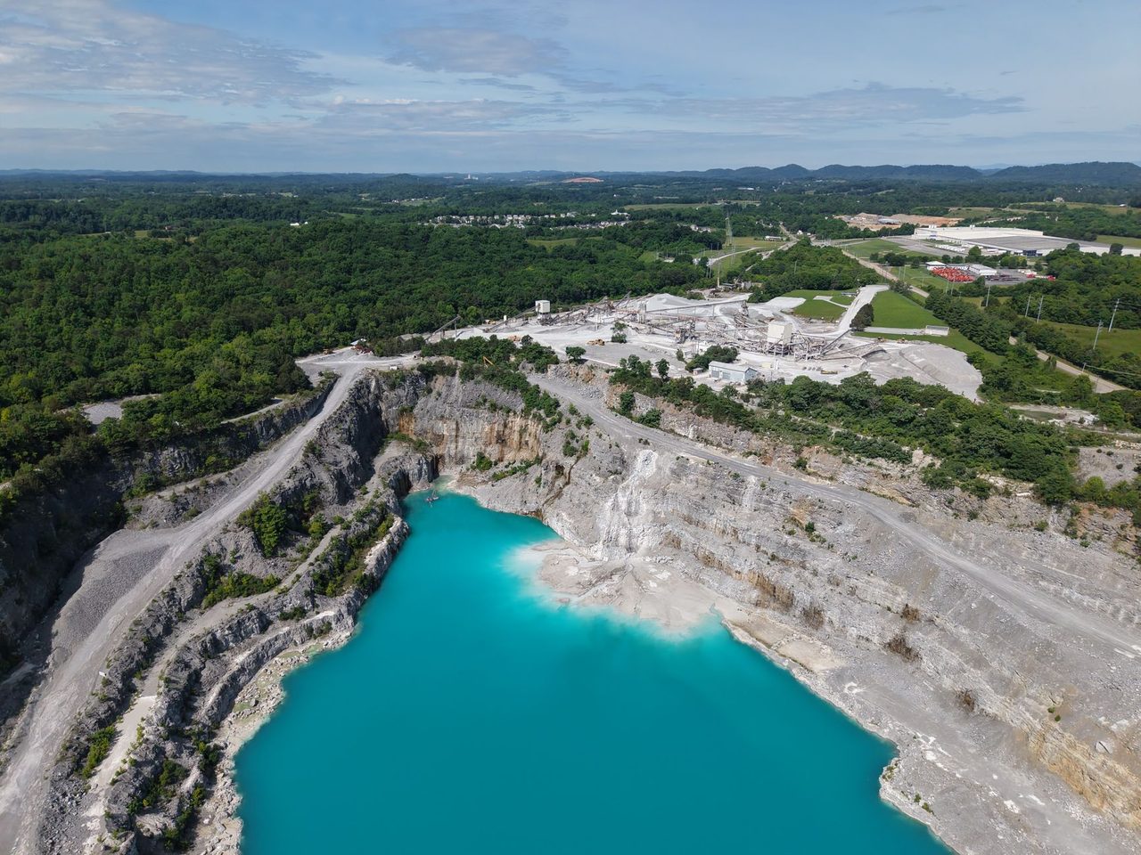 Aerial view of a quarry with stepped rock walls and a turquoise flooded pit