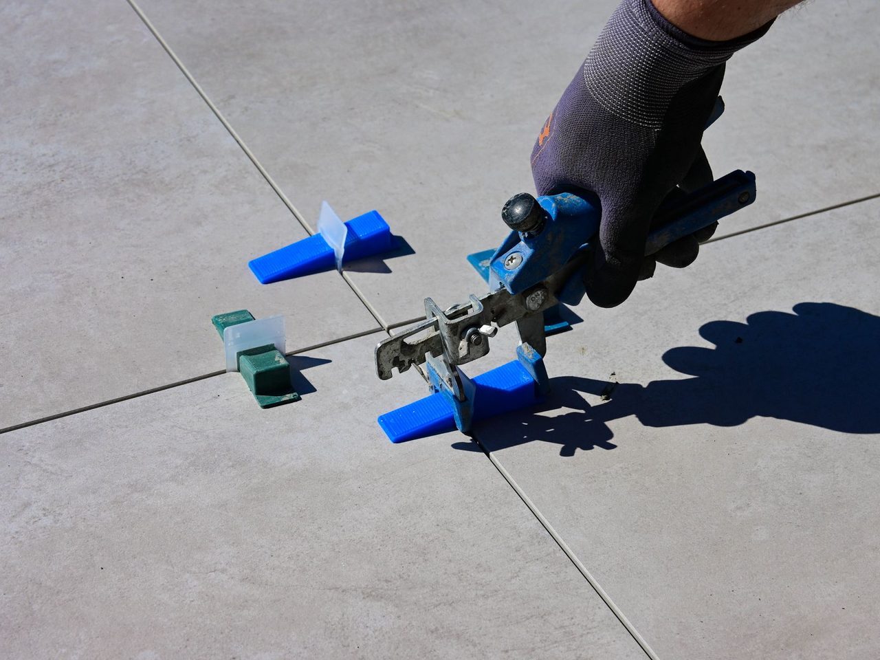 Gloved hand using a pliers-type tool to tighten tile leveling clips