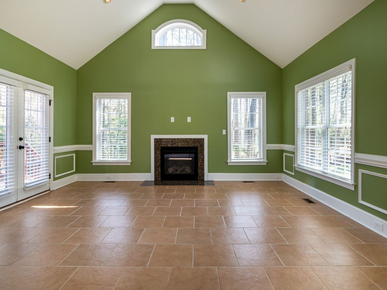Empty room with green walls, a fireplace and a terracotta-toned tile floor