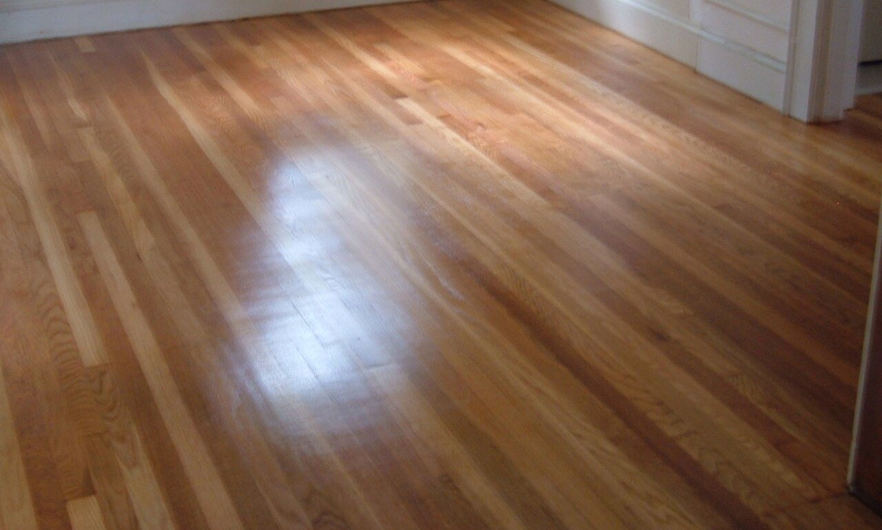 Glossy oak strip floor in an empty room with white baseboards and a doorway