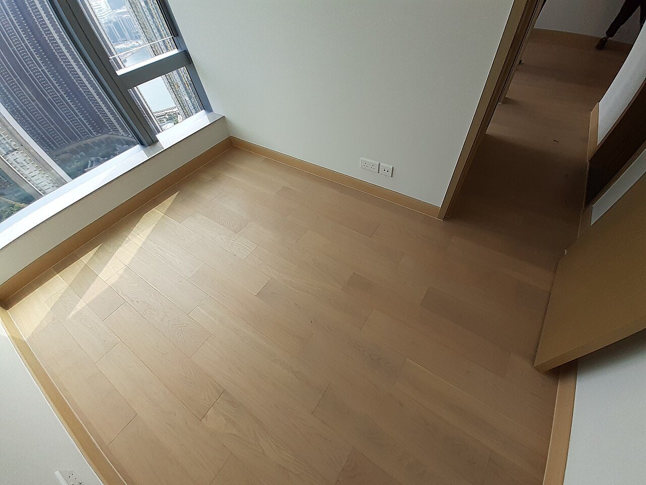 Empty apartment room with light oak floor planks, matching skirting boards and a doorway to a hall