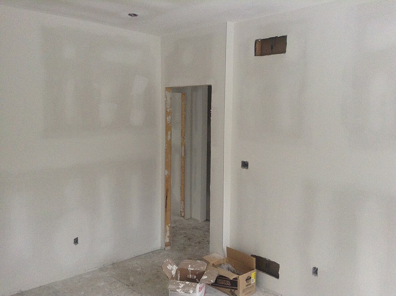 Freshly taped drywall walls and a doorway in a room under construction, with compound boxes on the bare subfloor