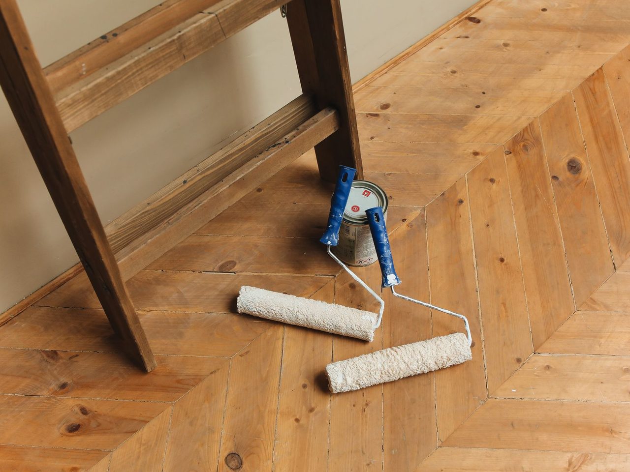 Paint rollers and a stepladder on a light wood floor