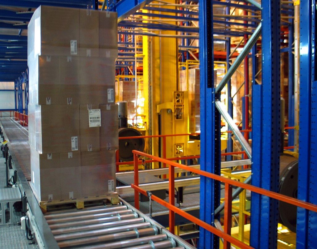 Pallet of wrapped cartons on a roller conveyor beside blue automated pallet racking