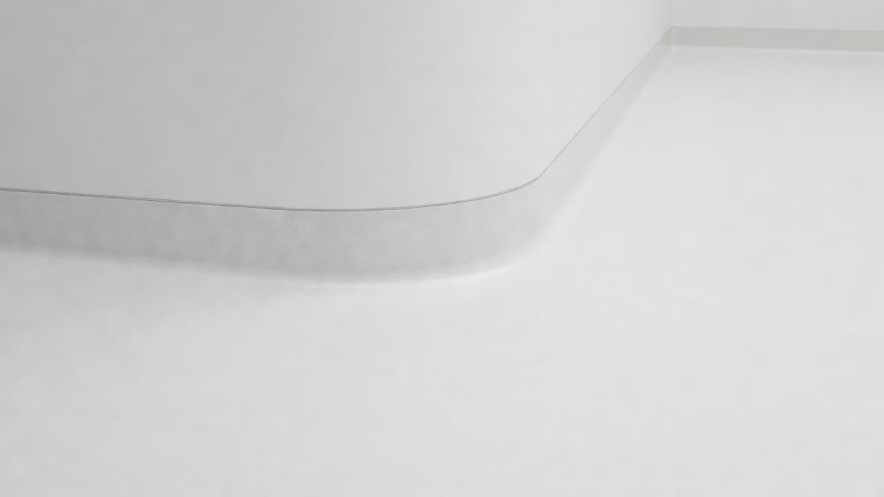 A close-up view of a curved vinyl floor-to-wall transition in a hospital room. The light reflects off the smooth heat-welded seam where two white vinyl sheets meet in a clean corner.