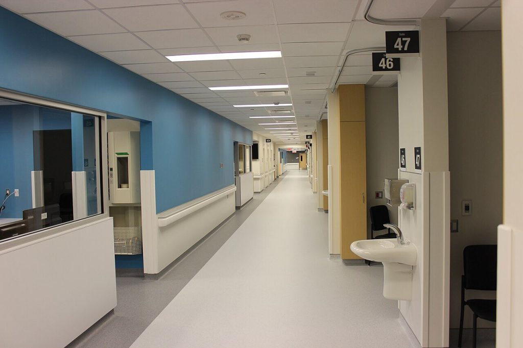 Emergency department corridor with light grey sheet vinyl, wall guards and a small handwash basin