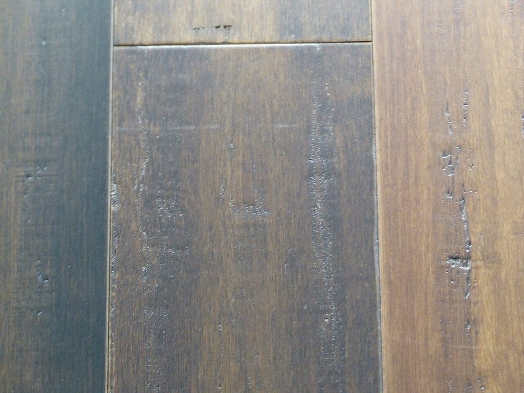 Close-up of dark hand-scraped floor planks with a scraped surface texture and an end joint