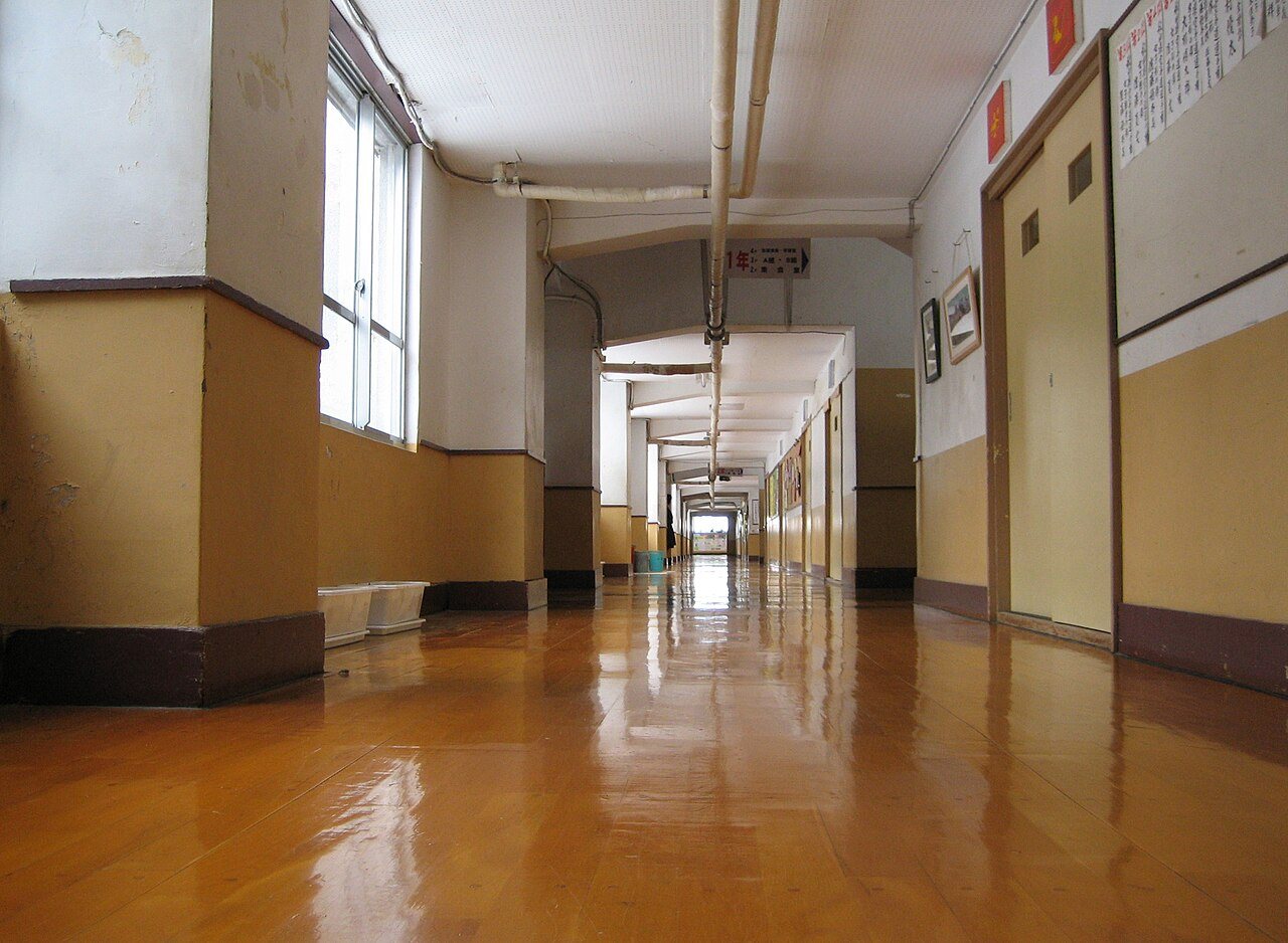 Long school hallway with a glossy honey-colored wooden floor running to a bright doorway